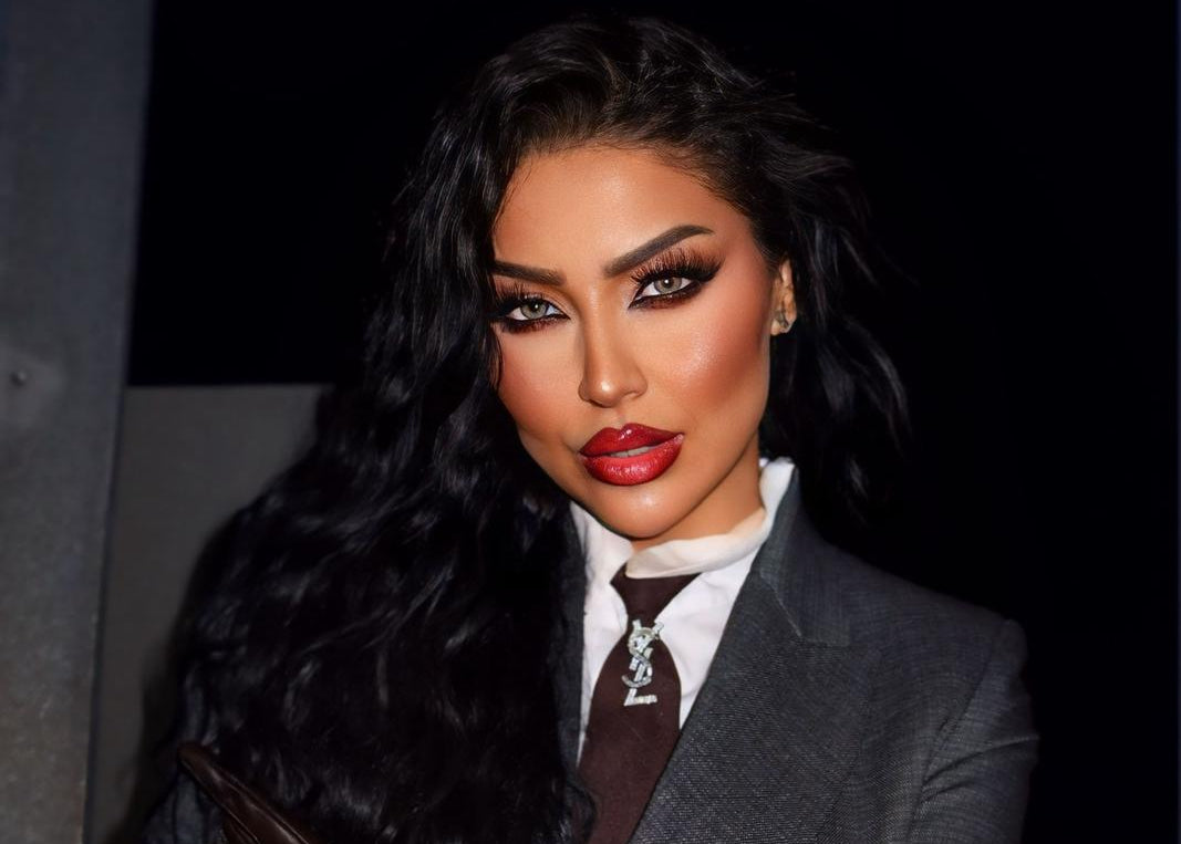 Woman in a gray suit with a fur stole and leather gloves against a dark background